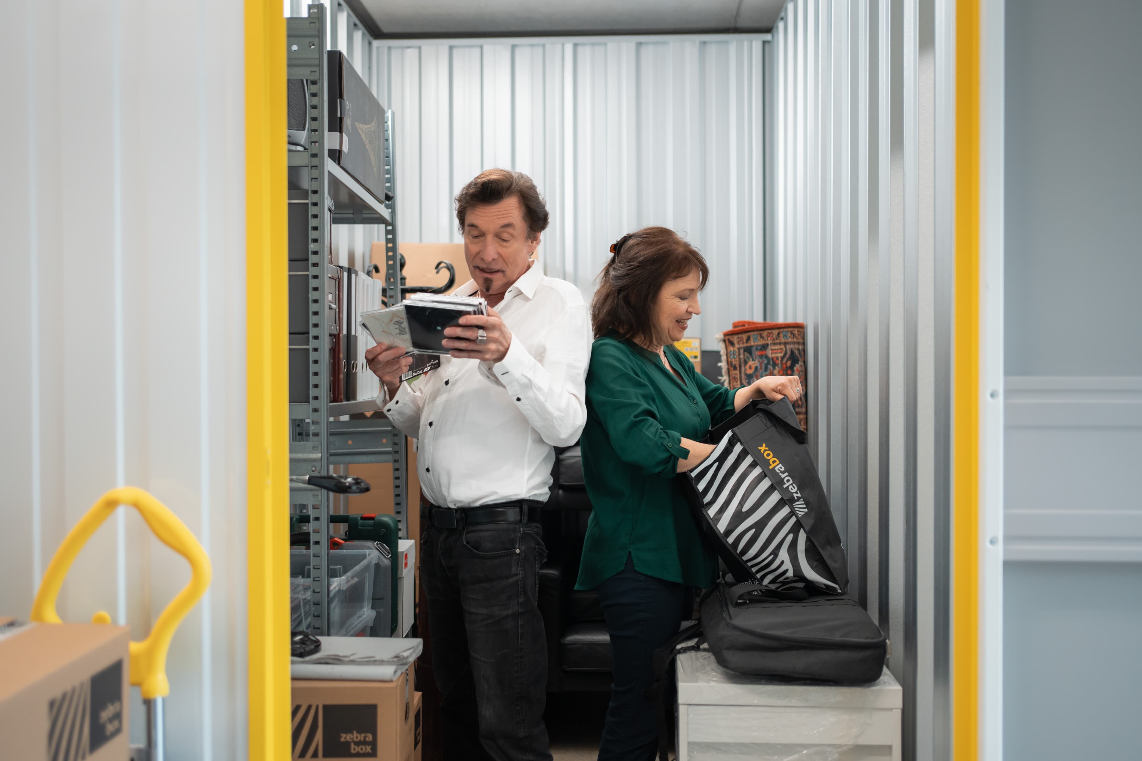 An elderly couple is standing back to back looking at stored items in their storage unit at Zebrabox.